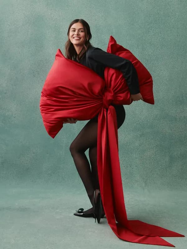Studio portrait, a model wrapped in a large red satin bow